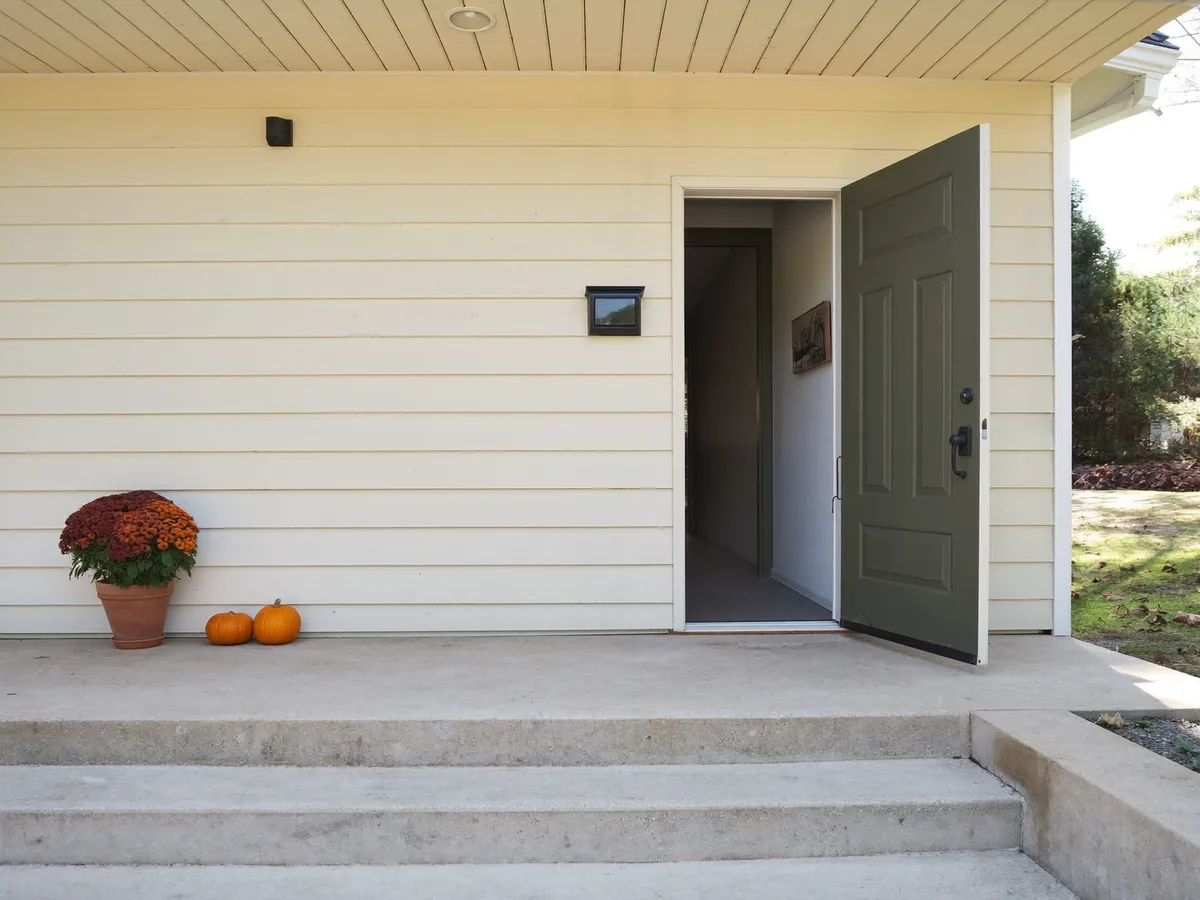 Small mum planter and two pumpkins placed far beside an open doorway with clear steps
